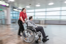 Eine VIAS-Mitarbeiterin führt einen Fluggast mit eingeschränkter Mobilität mit einem Rollstuhl über das Flughafengelände